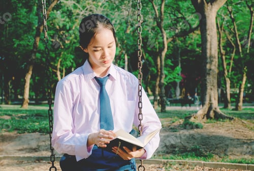Preview: Lovely Teenage Girl Wearing School Uniform Reading Book While Sitting On A Swing At The Park