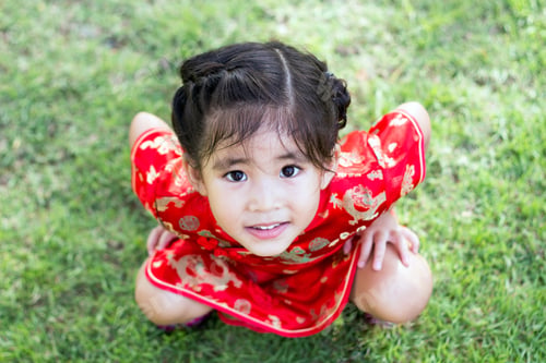Preview: Close Up Face Of Chinese Asian In Red Dress Sitting On Grass From Top View
