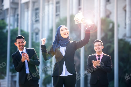 Preview: Successful Muslim Business Woman With Arms Up Holding A Trophy And Celebrating, With Teammates