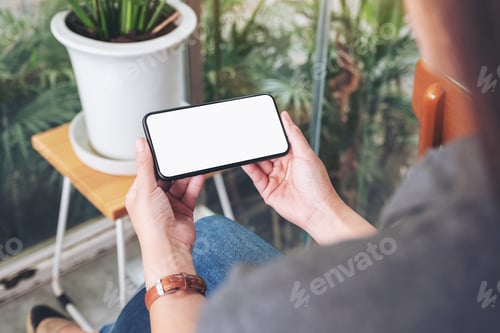 Preview: Mockup Image Of A Woman Holding And Using Black Mobile Phone With Blank Desktop Screen In Cafe