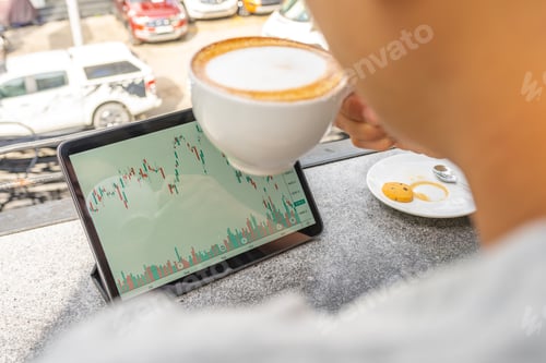 Preview: Businessman Having Hot Cappuccino And Watching Candlesticks Graph On Tablet