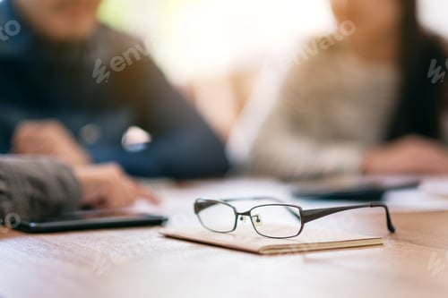 Preview: Close Up Image Of Black Eyeglasses On Notebook With Blur Businessman In Office