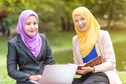 Preview: Muslim Women Entrepreneurs Having A Business Meeting By A Lake With A Laptop. Looking At The Camera