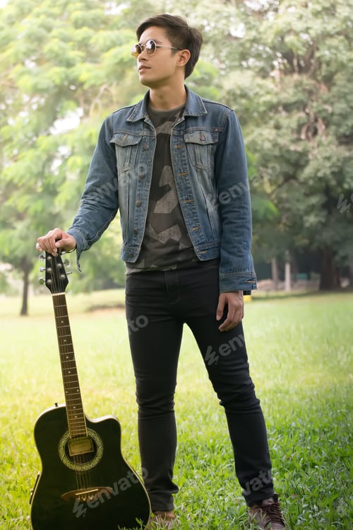 Preview: Young Man Holding A Guitar And Jumping In The Park.Asian Young Men Jump In Nature Playing Guitar
