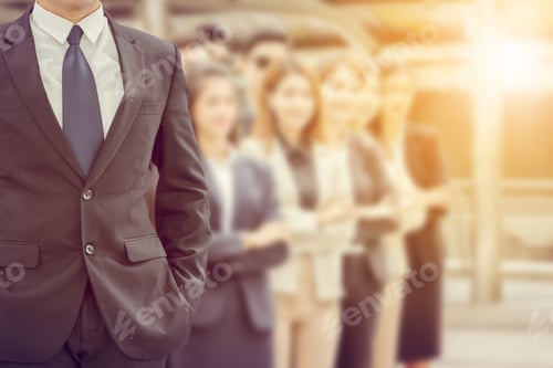 Preview: Close Up Of Businessman Standing With Hands In Pocket Over Blurry Success Business People Team