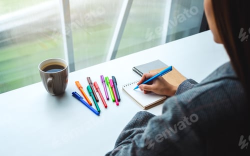 Preview: Closeup Image Of A Woman Writing On A Blank Notebook With Colored Pens And Coffee Cup On The Table