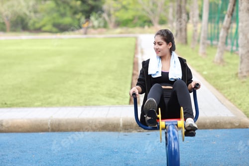 Preview: Happy Smiling Young Beautiful Asian Woman In Sportswear Relaxing On Public Exercise Machine. Cute