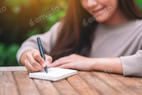 Preview: Closeup Image Of A Beautiful Woman Writing On Blank Notebook On Wooden Table In The Outdoors