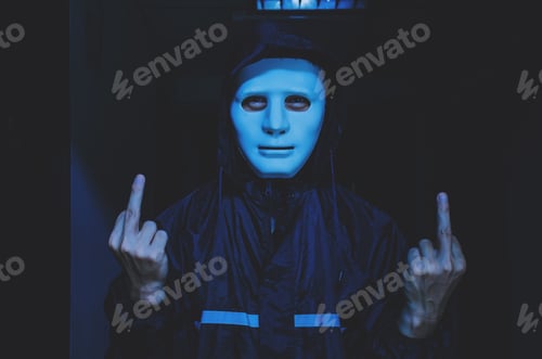 Preview: Unrecognizable Young Man In White Mask And Hoodie Showing Middle Finger At Camera.