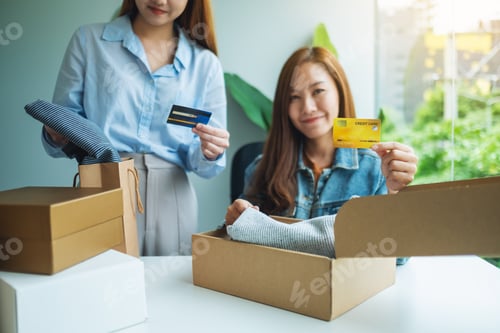 Preview: Two Women Holding And Using Credit Card For Online Shopping While Opening A Postal Parcel Box Of