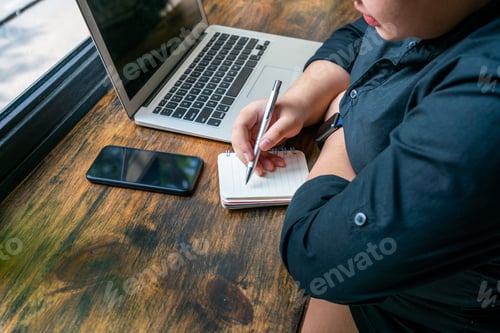 Preview: Woman Writing Notebook Next To Laptop At Wooden Working Table