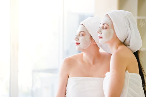 Preview: Beautiful Young Woman And Friend Spa Applying Cosmetic Mask Cream On Face Relaxing Receiving