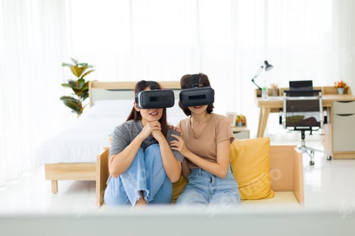Preview: Teenage Girls Who Are Intimate Friends Wearing Vr Glasses While Sitting On Sofa, Two Young Asian