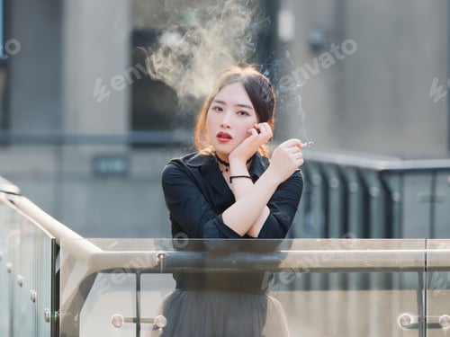 Preview: Portrait Of Beautiful Chinese Girl In Black Dress Smoking A Cigarette Outdoor In Sunny Day.