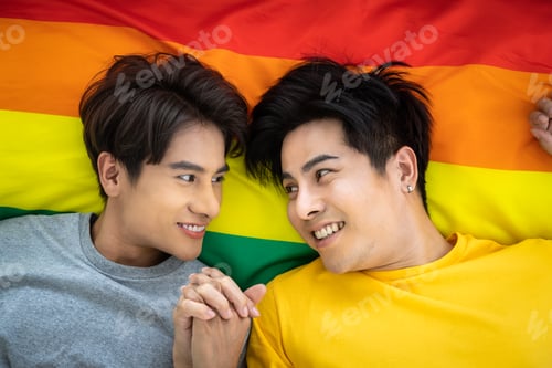 Preview: Happy Asian Homosexual Gay Couple Lying On Rainbow Pride Flag, Holding Hand. Lgbt Concept.