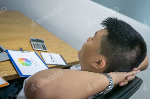 Preview: Young Businessman Relaxing At Office On The Chair, He Is Sleeping With Hands Behind Head