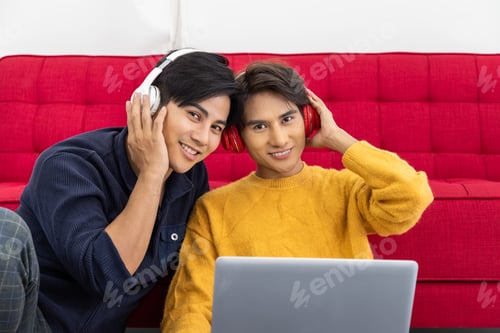 Preview: Young Asian Gay Couple Sitting On Sofa Using Laptop, Using Headphones Listen To Music Together