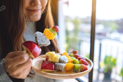 Preview: Closeup Image Of An Asian Woman Holding And Eating A Fresh Mixed Fruits On Skewers