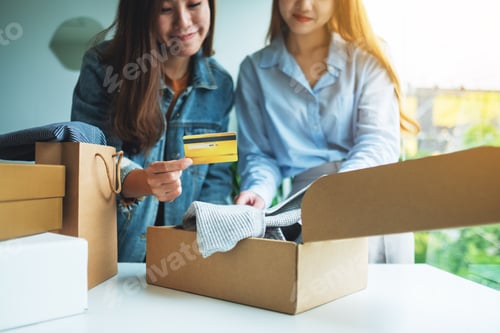 Preview: Two Women Holding And Using Credit Card For Online Shopping While Opening A Postal Parcel Box Of