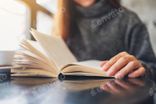 Preview: Closeup Image Of A Beautiful Woman Holding And Reading A Book With Coffee Cup On The Table