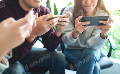 Preview: Group Of Young People Using And Plying Games On Mobile Phone While Sitting Together