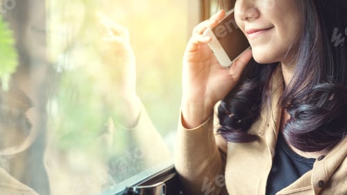 Preview: A Beautiful Asian Woman Looking Outside And Talking On Smart Phone In The Room With Reflections In