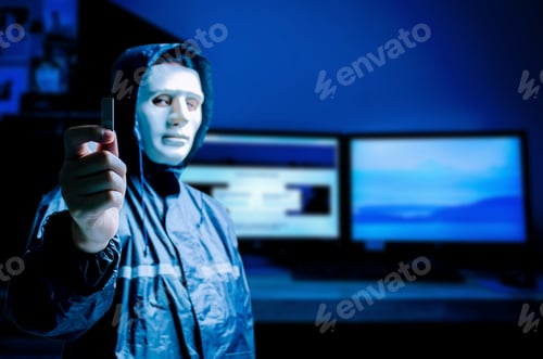 Preview: Anonymous Computer Hacker In White Mask And Hoodie. Obscured Dark Face Holds A Usb Flash Drive In