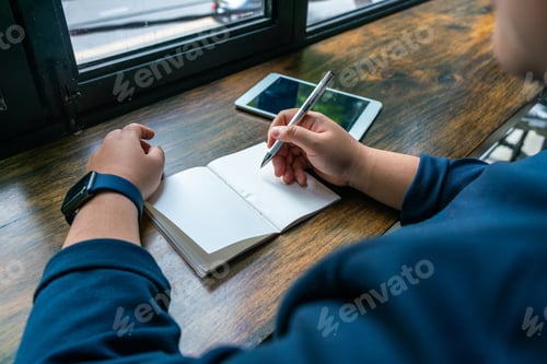 Preview: Woman Holding Pen And Writing On Notebook Next To Tablet