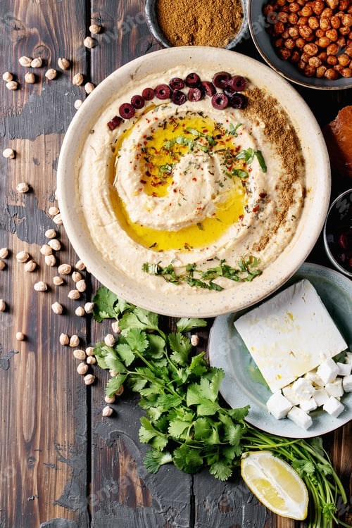 Vista previa: Hummus With Olive Oil And Ground Cumin In Ceramic Bowl Served With Lemons, Olives, Feta Cheese