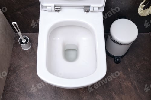Preview: Clean Toilet Bowl With Drain Hole, Top View. Toilet Brush And Trash Can On Black Tiles