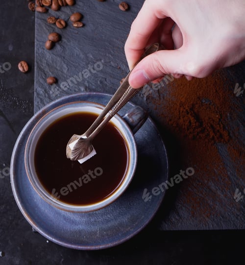 Preview: A Cup Of Coffee On Black Slate Board With Coffee Beans, Sugar And Tiny Sugar Tongs. Male Hands