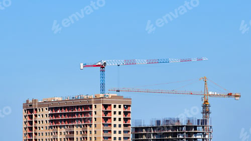 Preview: Two Brick Buildings Are Being Built Using Two Tower Cranes Against A Clear Sky Background.