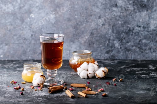Preview: A Black Metal Teapot And A Cup Of Tea In Glass Cup Served With Honey And Kotton Flower Over Dark