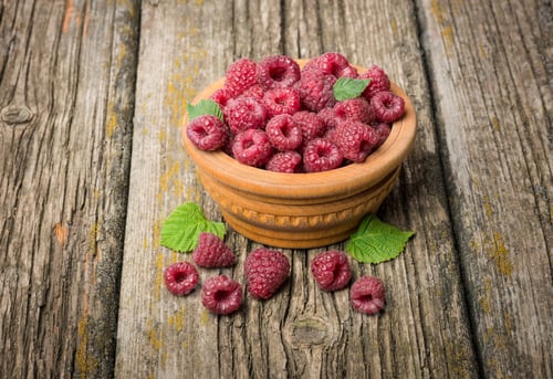 Preview: Ripe Raspberries With Green Leaves In A Bowl On A Wooden Table