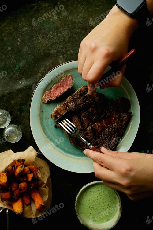 Preview: Grilled Rib Eye Steak Dinner Served With Sweet Potato Fries. Woman Cutting Steak. Home Made Dinner