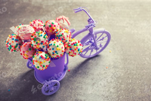 Preview: Cake Pops In Decorative Bicycle On Grey Slate Background. Selective Focus. Toned Image.