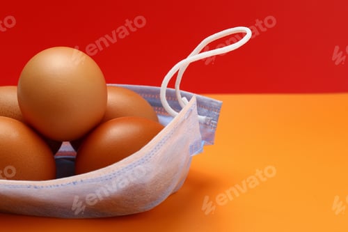 Preview: Chicken Eggs And Medical Mask On A Yellow Background. Metaphor With A Package From The Market Or A