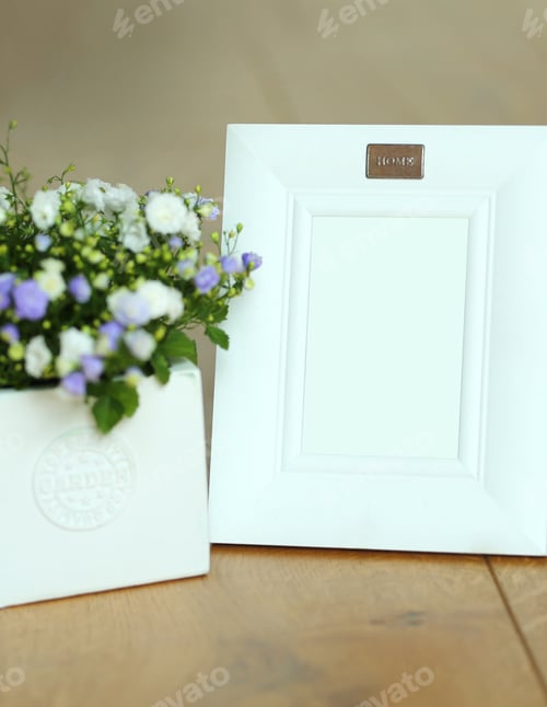 Preview: White Frame For Photo And Lilac Flowers In A White Pot Stand On A Wooden Surface.