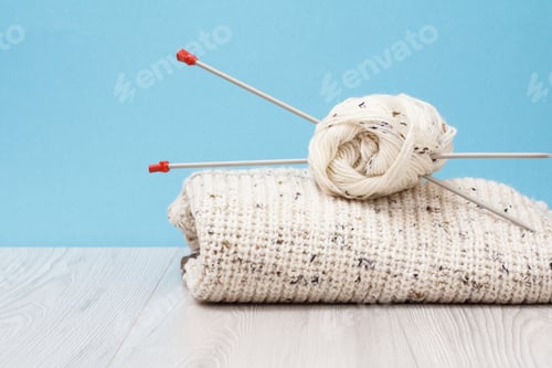 Vista previa: Pullover And Skeins Of Yarn With Metal Knitting Needles On Gray Boards And A Blue Background