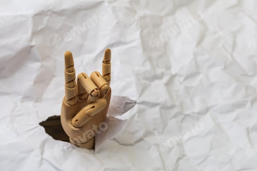 Preview: A Wooden Hand Breaks Through The Crumpled Paper Background And Demonstrates The Goat Gesture