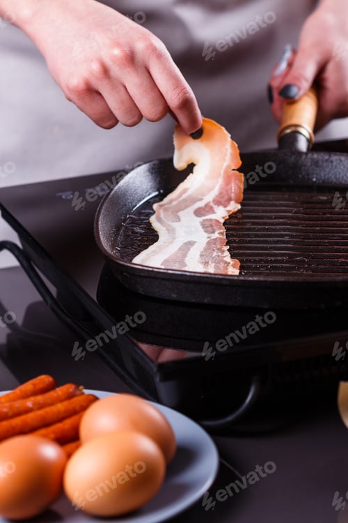 Preview: Young Woman In A Gray Apron Fries Bacon