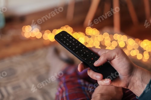 Preview: A Black Tv Remote Controller In A Man'S Hand, Legs In Check Pyjamas, Sitting On A Couch In A Cosy