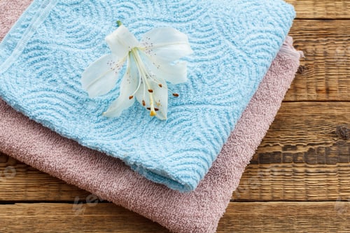 Preview: Blue And Pink Soft Terry Towels With White Lily Flower On Old Wooden Boards. Top View.