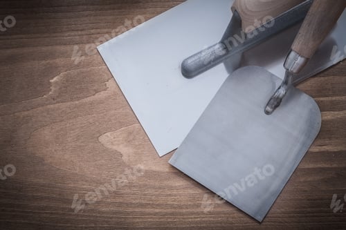 Preview: Stainless Plastering And Bricklaying Trowels On Wooden Board Construction Concept.