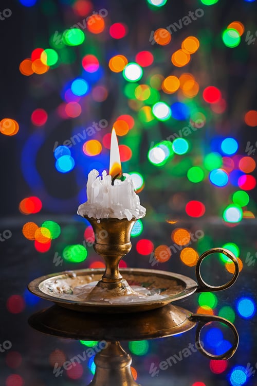 Preview: Glowing Old Candle In Wintage Candlestick On Surface Of Mirror With Multycolored Bokeh