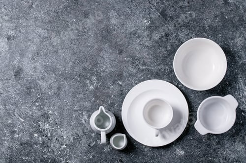 Preview: Variety Of Empty White Ceramic Plates And Bowls Over Dark Texture Background. Top View, Flat Lay