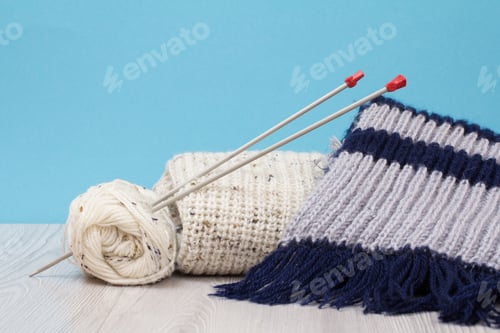 Vista previa: Pullover, Scarf And Skeins Of Yarn With Metal Knitting Needles On Gray Boards And A Blue
