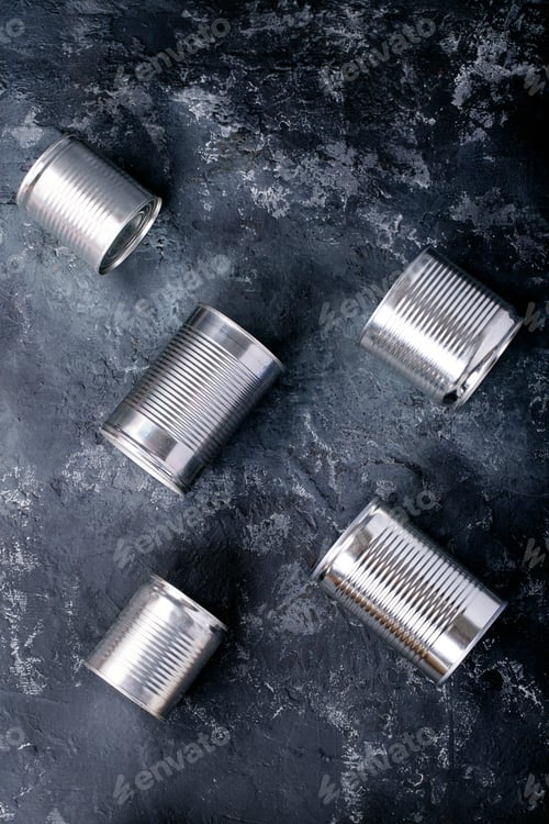 Preview: Canned Food In Metal Cans Over Dark Texture Background. Copy Space. Food Supply Concept. Top View