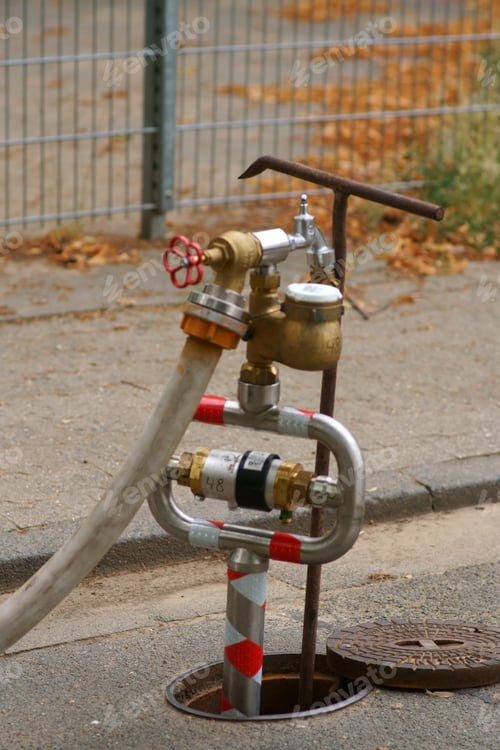 Preview: A Water Pumping Station With Water Pipes And A Water Meter At The Curb Of A Walkway.