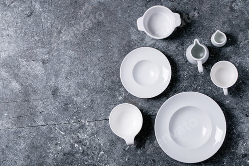 Preview: Variety Of Empty White Ceramic Plates And Bowls Over Dark Texture Background. Top View, Flat Lay
